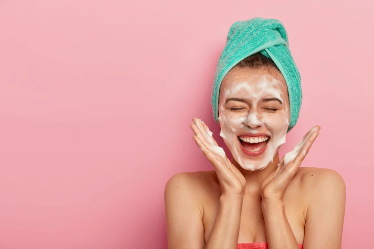 happy-joyous-young-girl-spreads-palms-face-washes-face-with-soap-has-fun-bathroom-pampers-skin-wears-wrapped-towel-head-expresses-positive-emotions_273609-33473